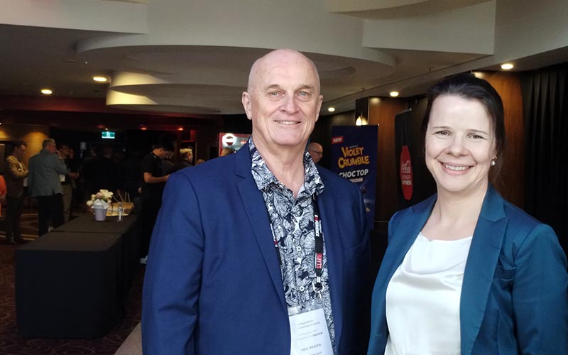 Two people standing next to each other with ICA conference booths in the background